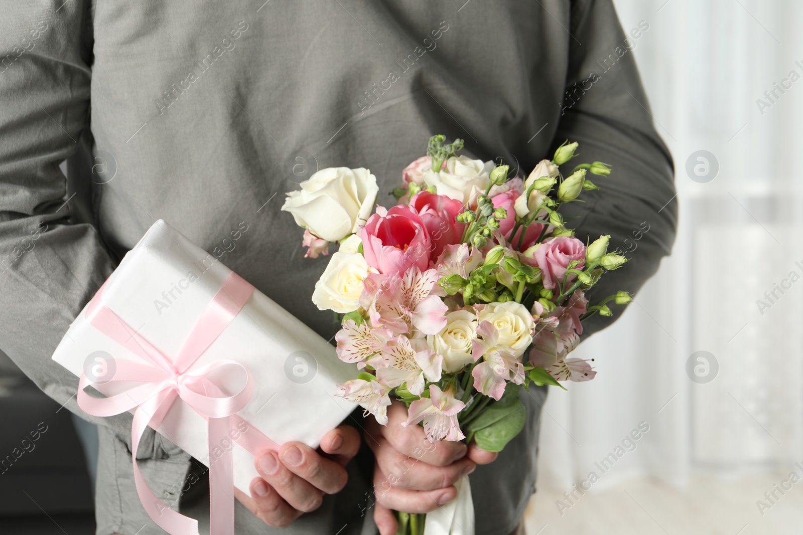 Photo of Man hiding bouquet of flowers and present indoors, closeup