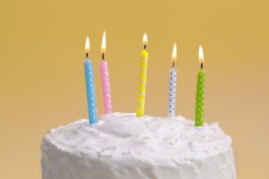 Photo of Delicious cake with cream and burning candles on yellow background, closeup