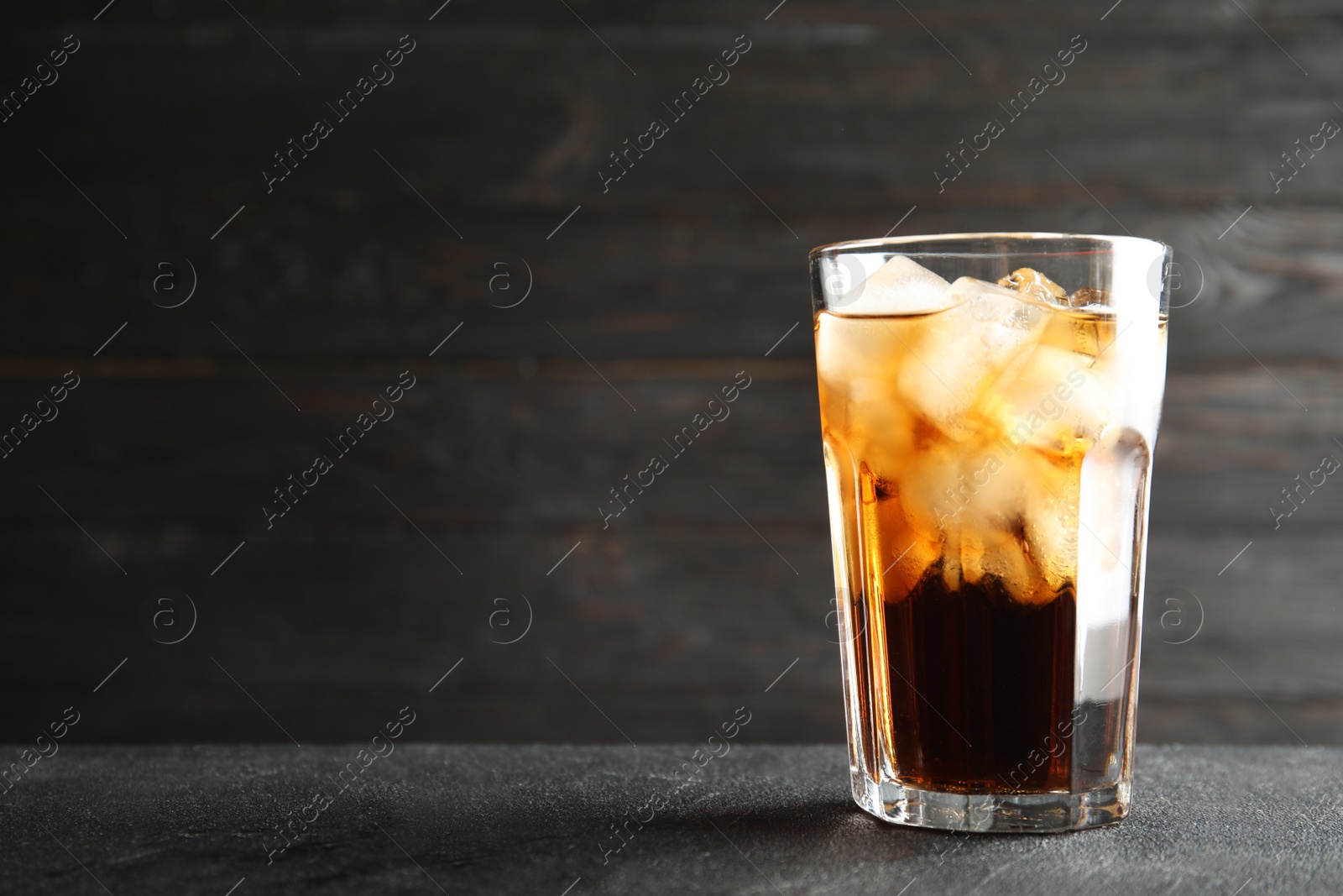 Photo of Glass of refreshing cola with ice cubes on table. Space for text