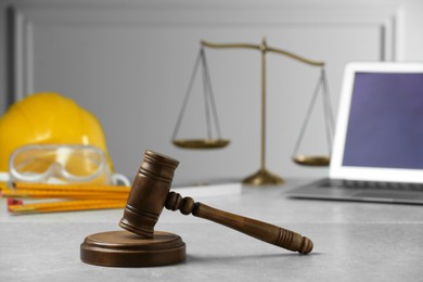 Photo of Construction and land law concepts. Judge gavel, scales of justice, safety glasses, protective helmet with laptop on light grey table