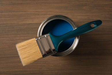 Photo of Can of blue paint and brush on wooden background, top view