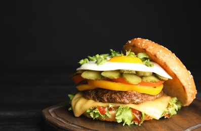 Photo of Tasty burger with fried egg on board against dark background, space for text