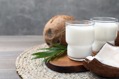 Glasses of delicious coconut milk, palm leaf and coconuts on wooden table, space for text