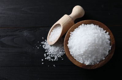 Organic salt in bowl and scoop on black wooden table, top view. Space for text