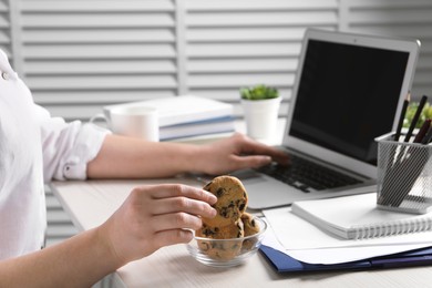 Photo of Office worker taking chocolate chip cookie from bowl at workplace, closeup