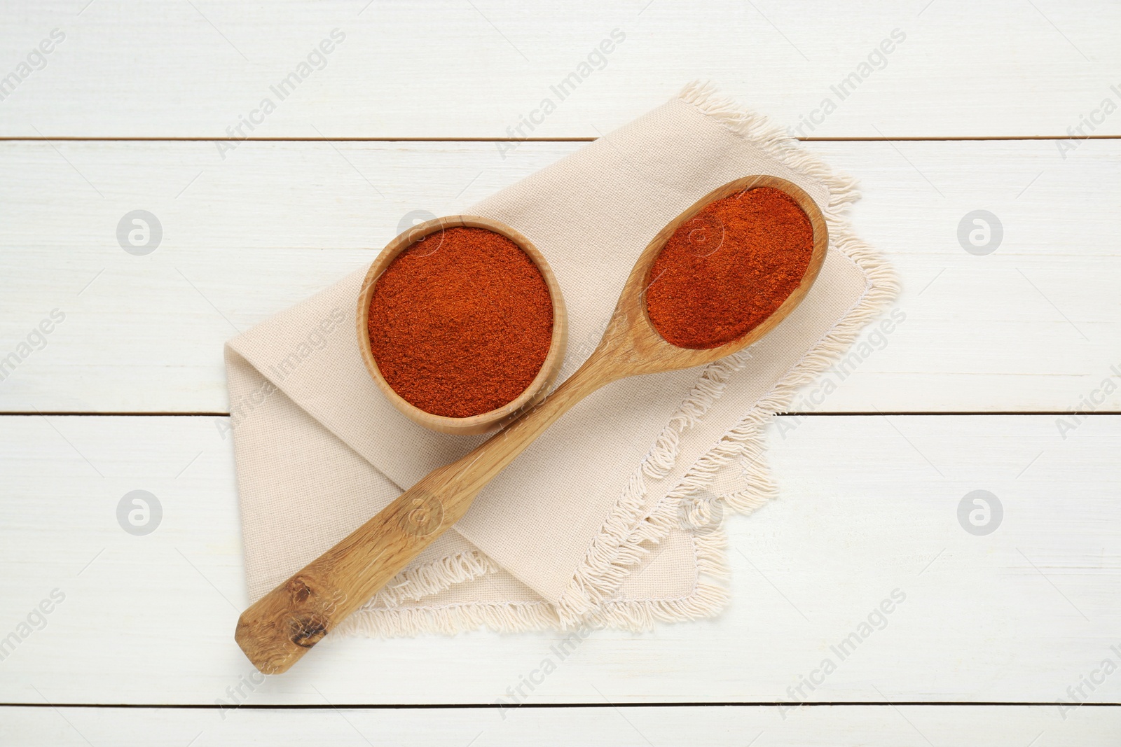 Photo of Bowl and spoon with aromatic paprika powder on white wooden table, flat lay