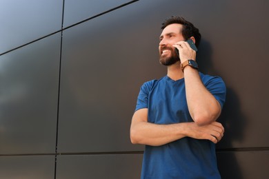 Photo of Happy man talking on phone near grey wall. Space for text