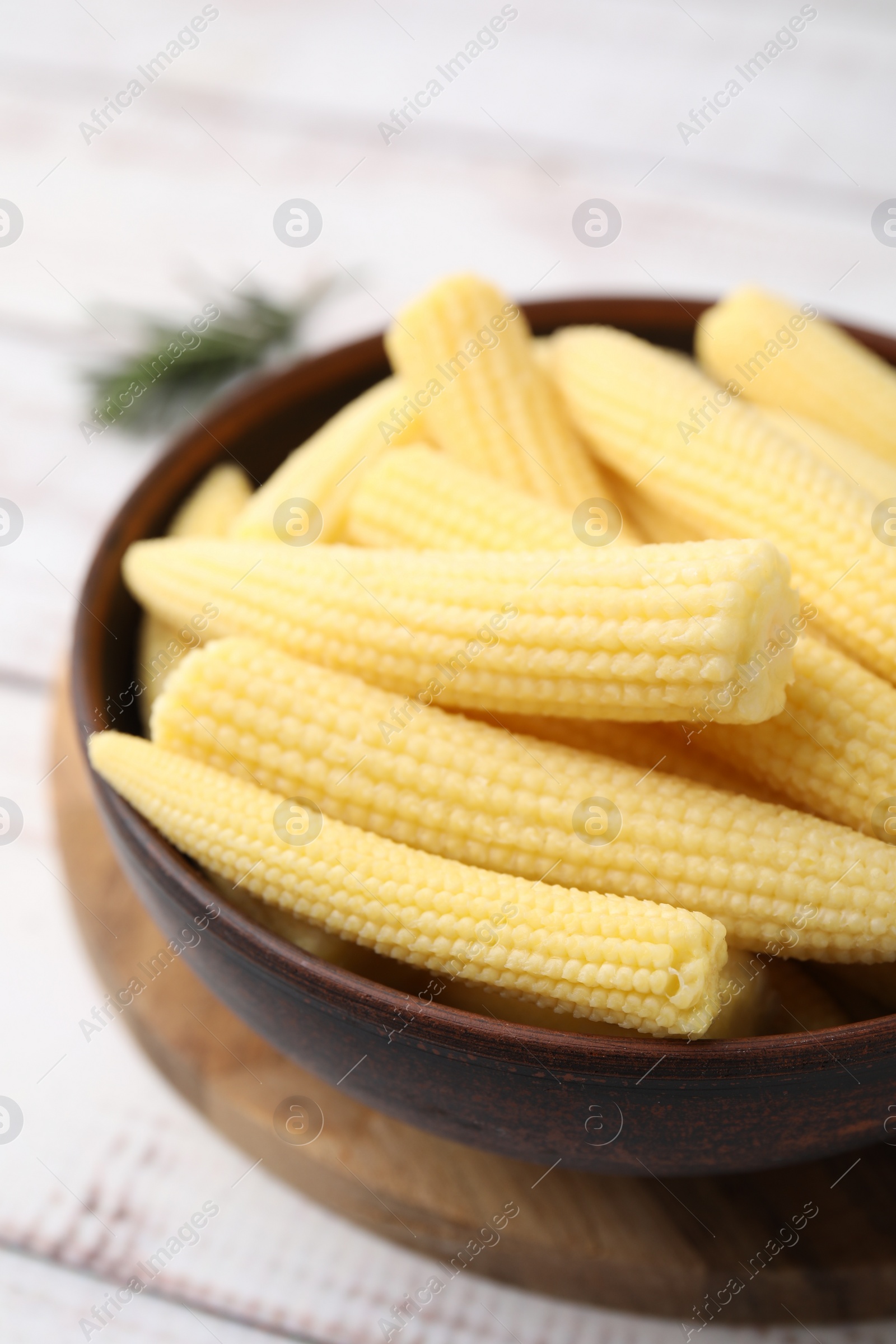 Photo of Tasty fresh yellow baby corns in bowl on white wooden table, closeup