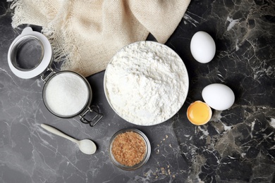 Photo of Bowl with flour, eggs and sugar on grey background, top view