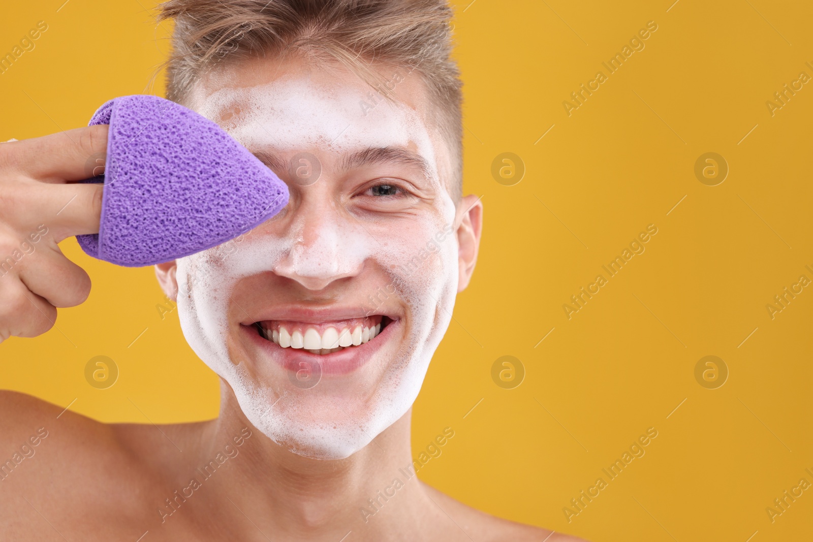 Photo of Happy young man washing his face with sponge on orange background. Space for text