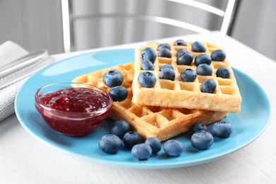Photo of Delicious waffles with blueberries served on white table, closeup