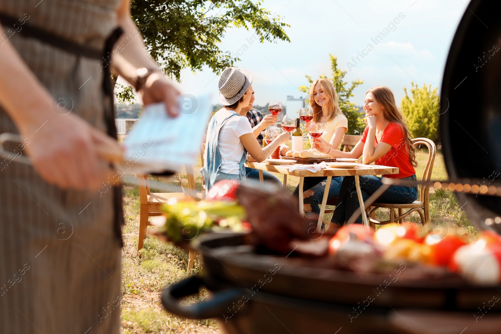 Photo of Young people with glasses of wine at table outdoors. Summer barbecue