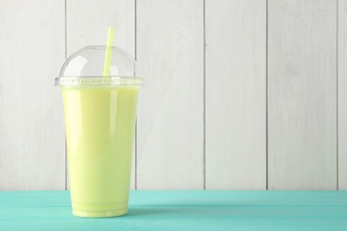 Photo of Tasty smoothie in plastic cup on light blue table against white wooden wall. Space for text