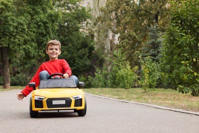 Photo of Cute little boy driving children's car outdoors. Space for text