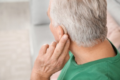 Photo of Mature man adjusting hearing aid at home, closeup