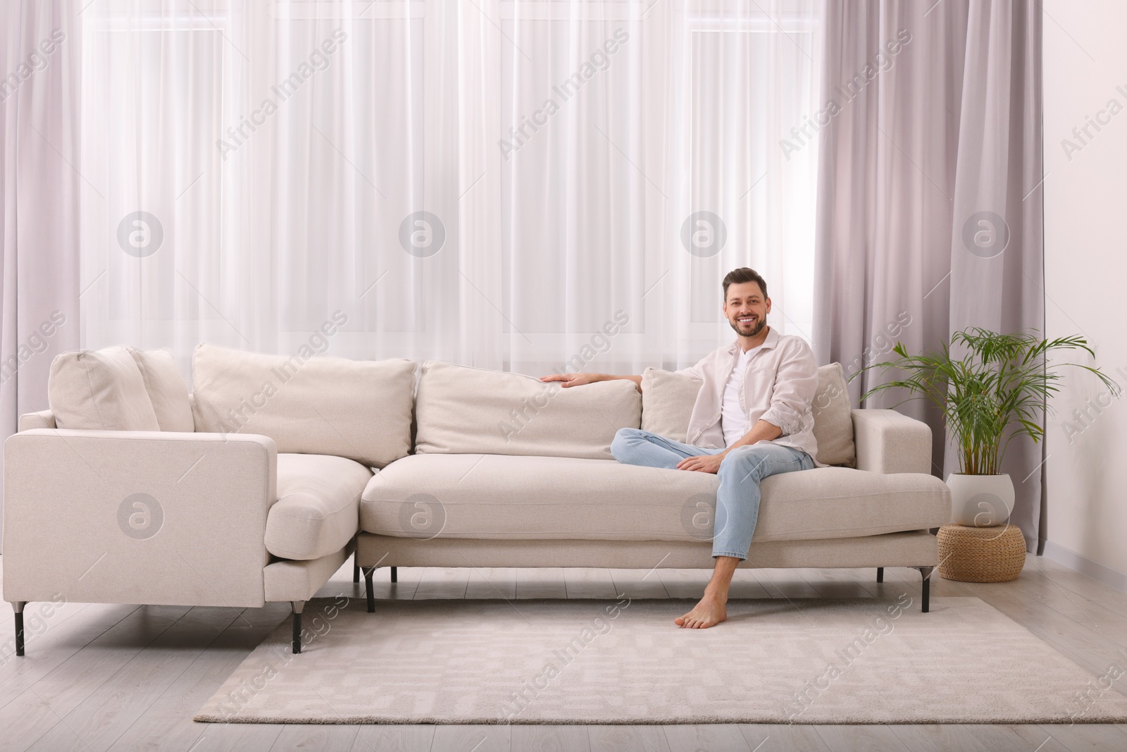 Photo of Happy man resting on sofa near window with beautiful curtains in living room