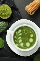 Photo of Delicious matcha latte, powder, leaves and whisk on dark table, flat lay