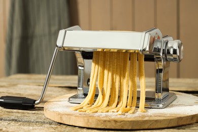 Pasta maker with raw dough on wooden table