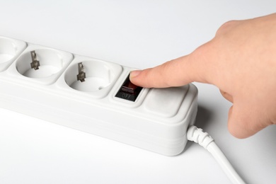 Woman pressing power button of extension cord on white background, closeup. Electrician's equipment