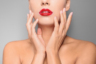 Photo of Beautiful young woman with red glossy lips on gray background, closeup