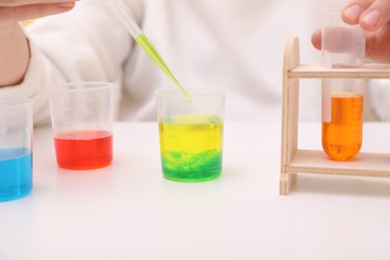 Girl mixing colorful liquids at white table indoors, closeup. Chemical experiment set for kids