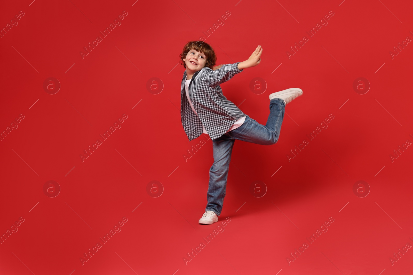 Photo of Happy little boy dancing on red background