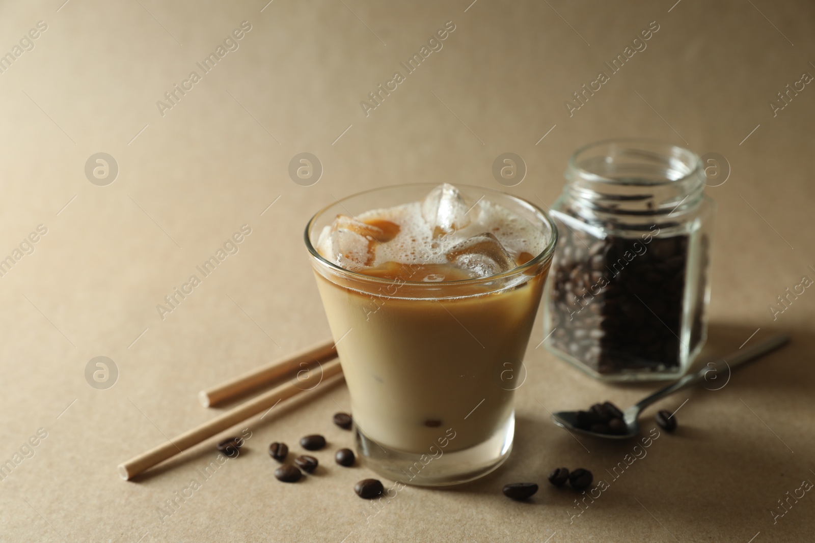 Photo of Refreshing iced coffee with milk in glass, straws and beans on beige background, closeup