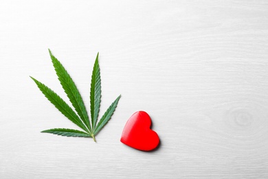 Photo of Green hemp leaf and red heart on white wooden background, flat lay. Space for text