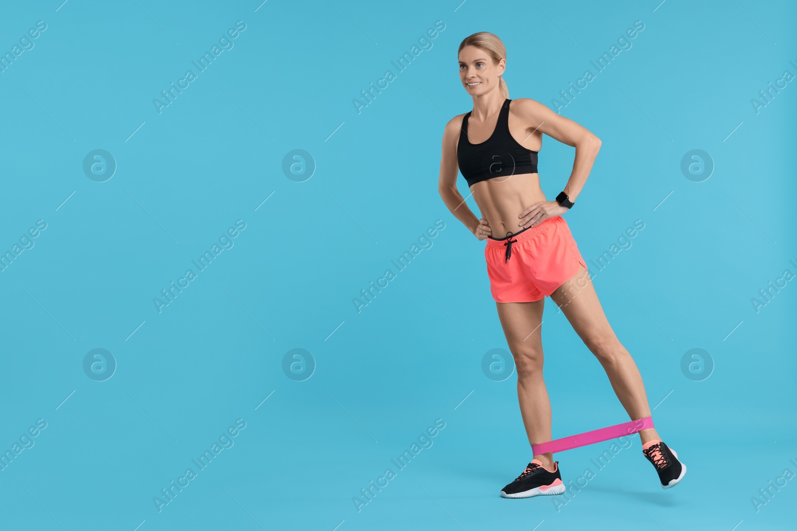 Photo of Woman exercising with elastic resistance band on light blue background. Space for text