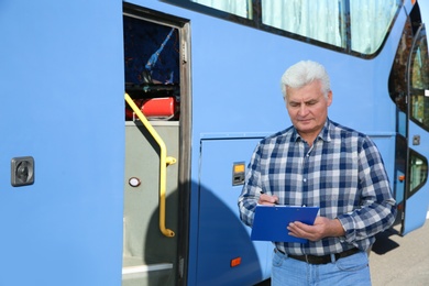 Professional driver with clipboard near bus. Passenger transportation