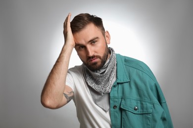 Fashionable young man in stylish outfit with bandana on grey background