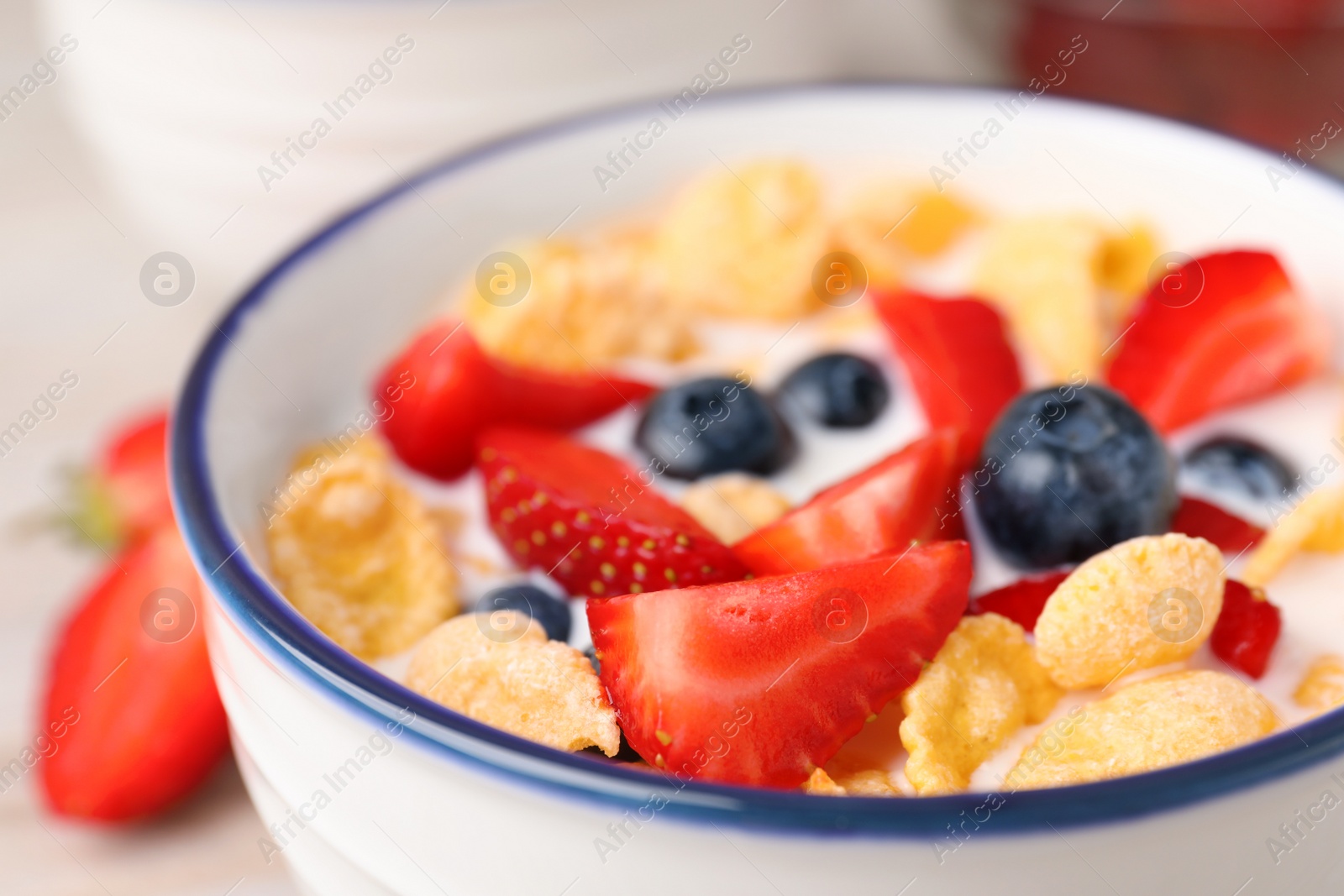 Photo of Bowl of tasty crispy corn flakes with milk and berries, closeup