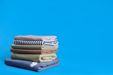 Photo of Stack of clean bed sheets on blue background. Space for text