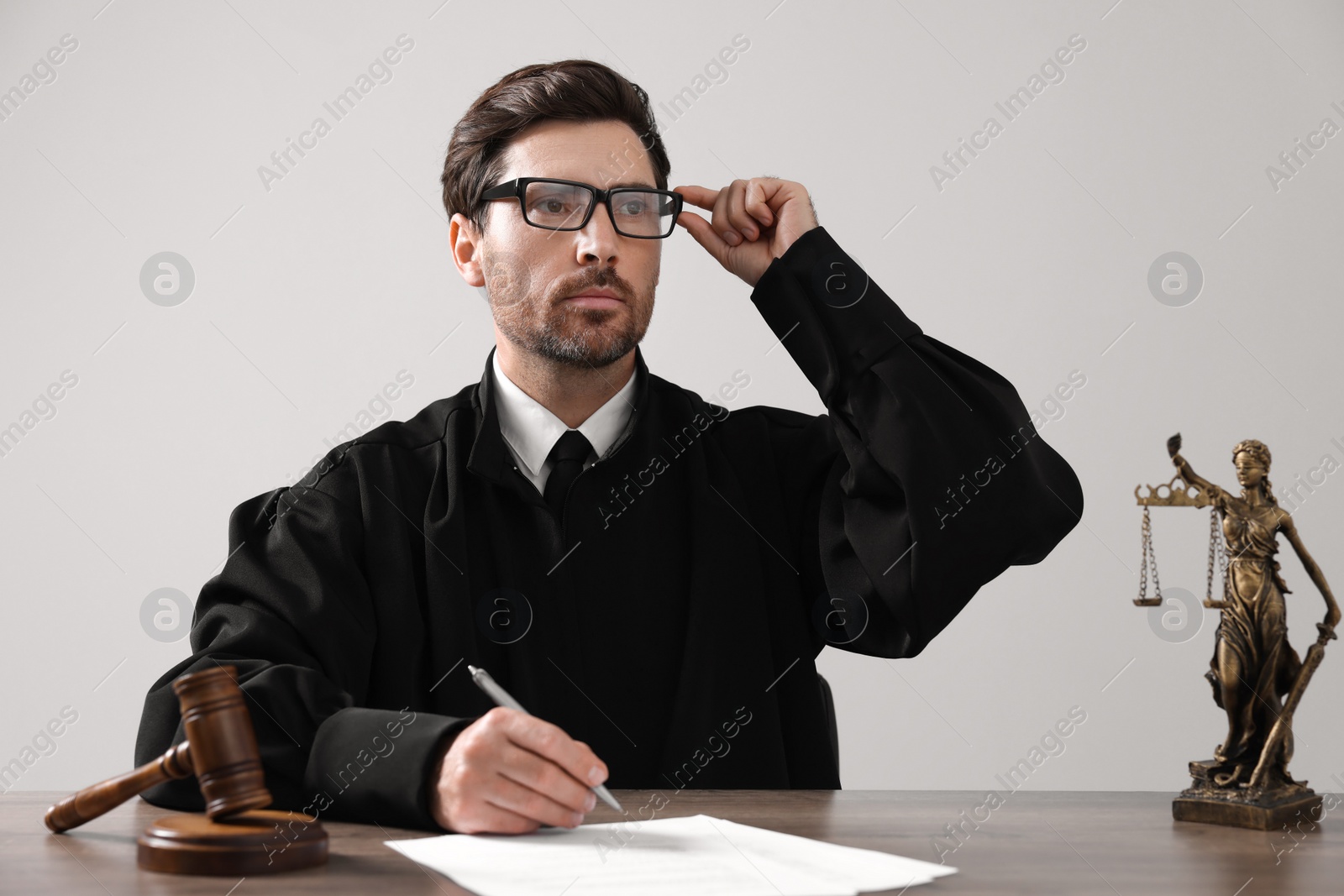 Photo of Judge with gavel and papers sitting at wooden table against light grey background