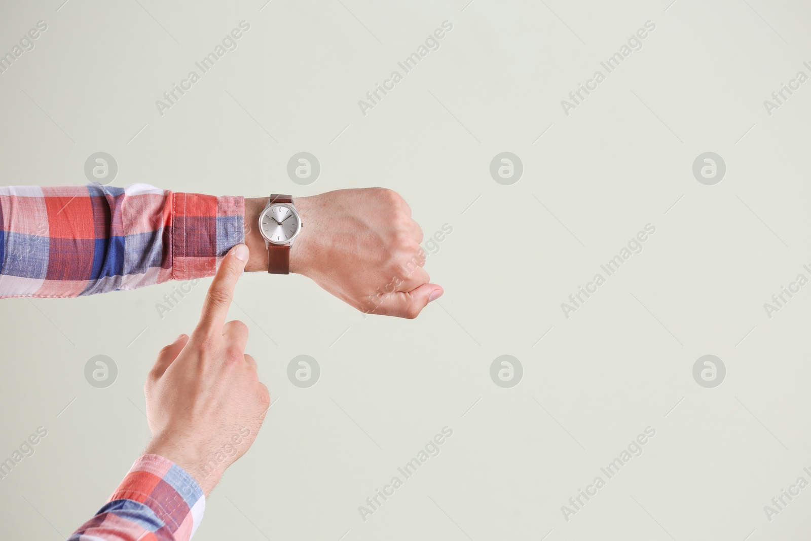 Photo of Young man with wristwatch on grey background. Time concept