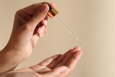 Photo of Woman applying cosmetic serum onto her finger on beige background, closeup. Space for text