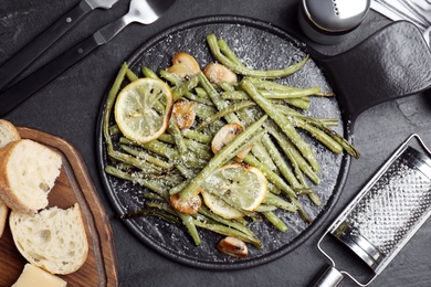 Photo of Delicious baked green beans served on black table, flat lay