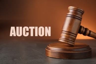 Image of Auction. Wooden gavel on grey textured table against brown background