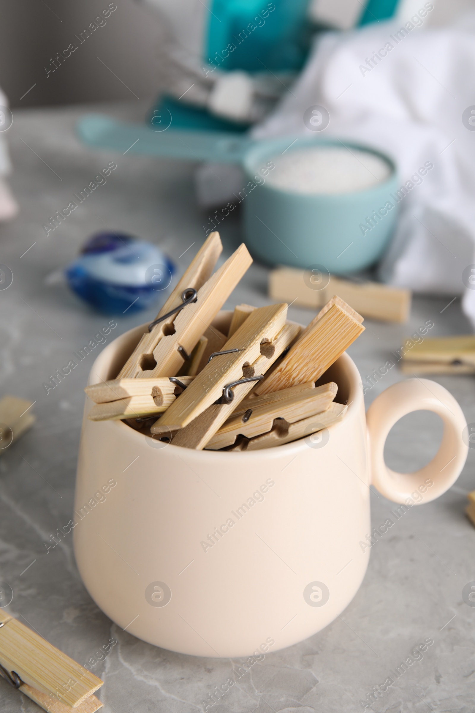 Photo of Many wooden clothespins in cup on grey marble table