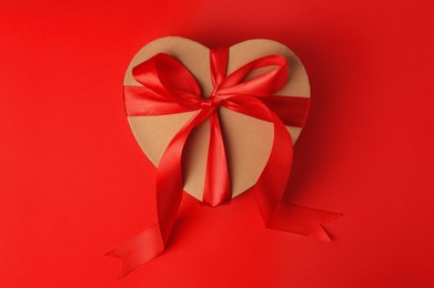 Photo of Beautiful heart shaped gift box with bow on red background, top view