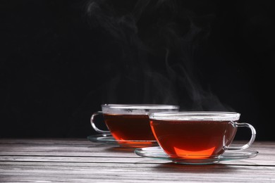 Glass cups with tea on wooden table against black background, space for text