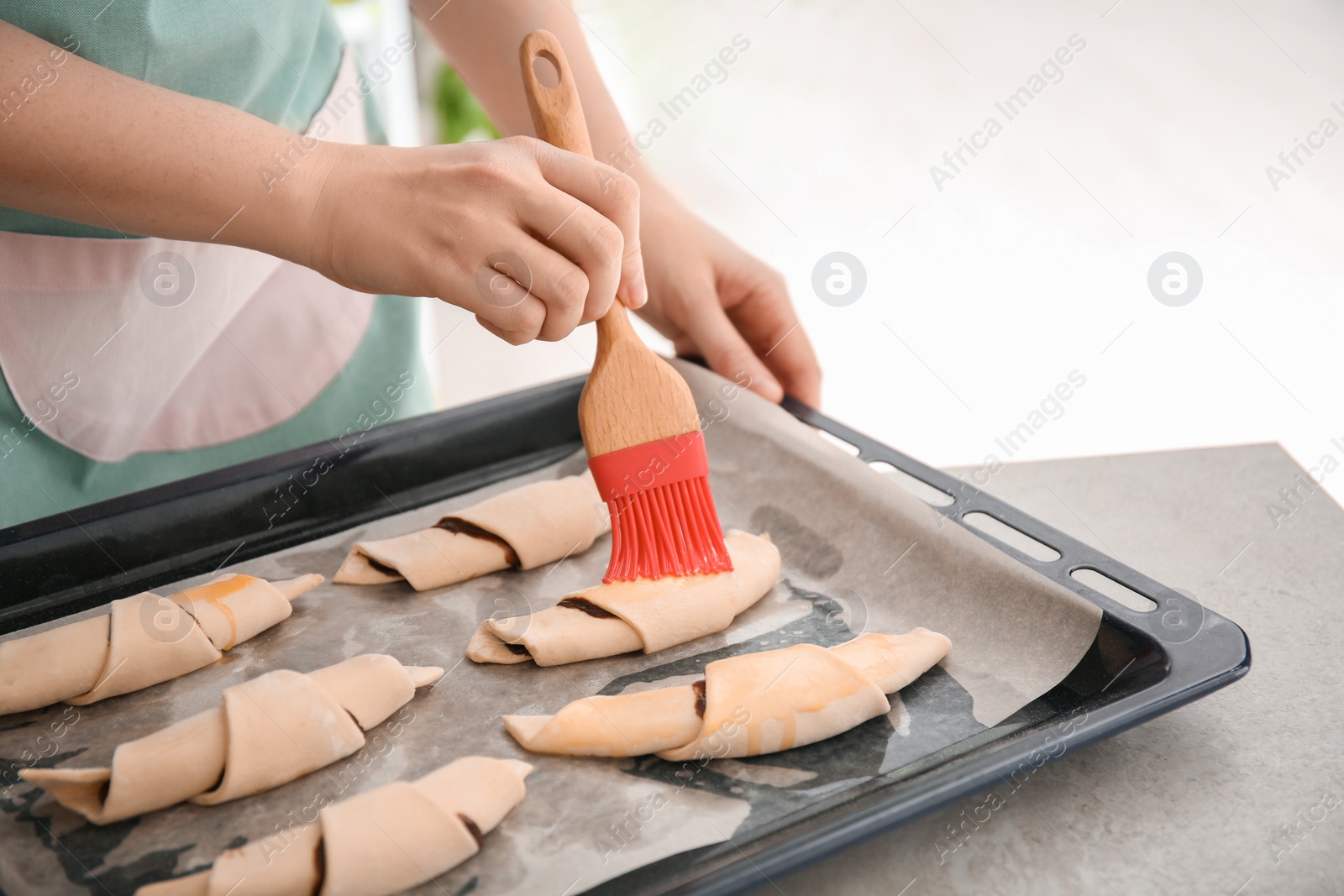 Photo of Woman spreading egg yolk on croissants, closeup