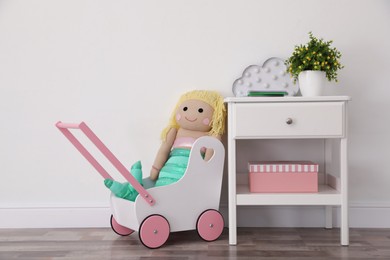 Photo of Toy stroller with doll and stand near light wall in baby room. Interior design