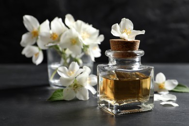 Photo of Jasmine essential oil and fresh flowers on dark grey table, space for text