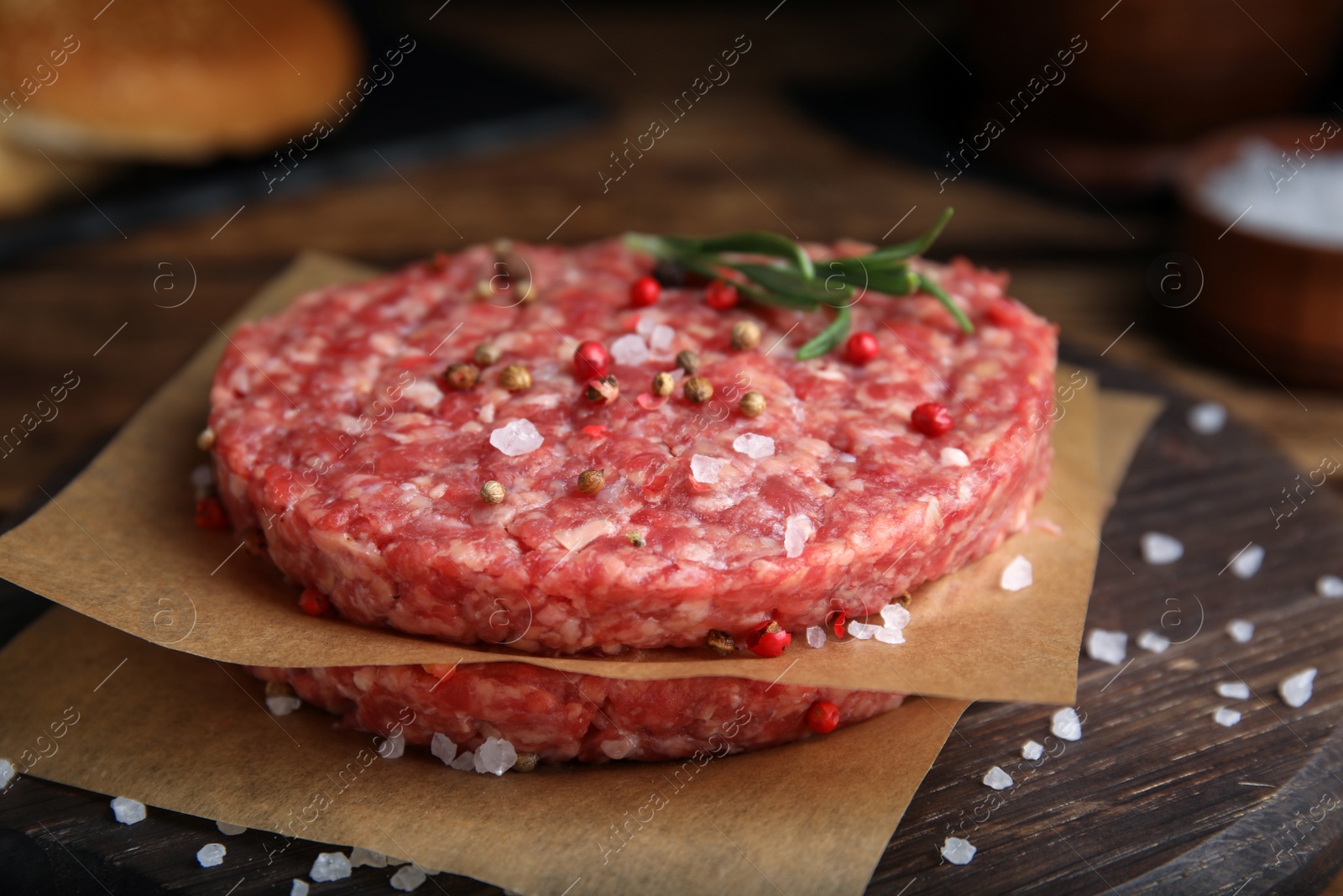 Photo of Raw hamburger patties with rosemary and spices on wooden board, closeup