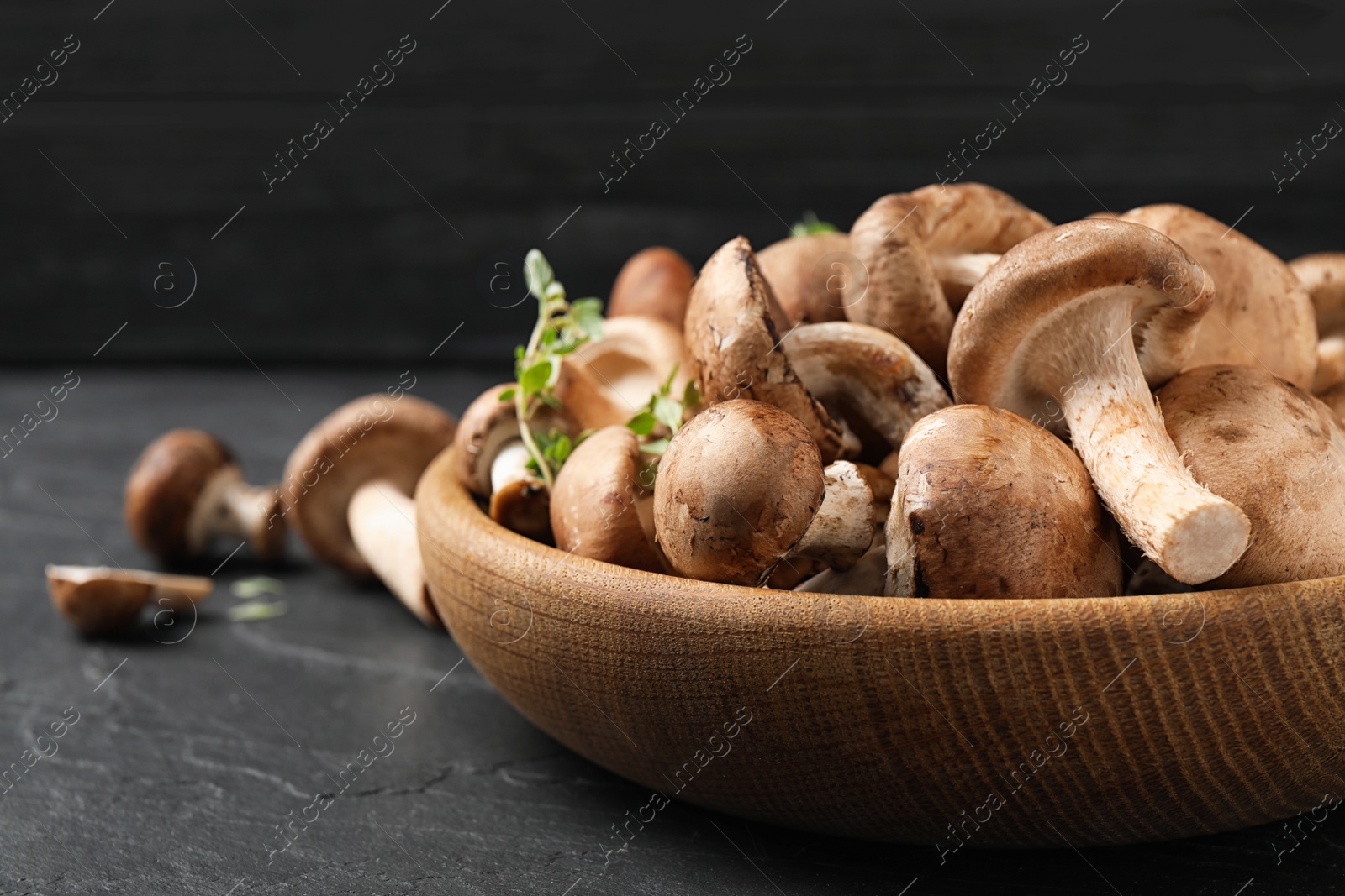 Photo of Fresh wild mushrooms in bowl on black table