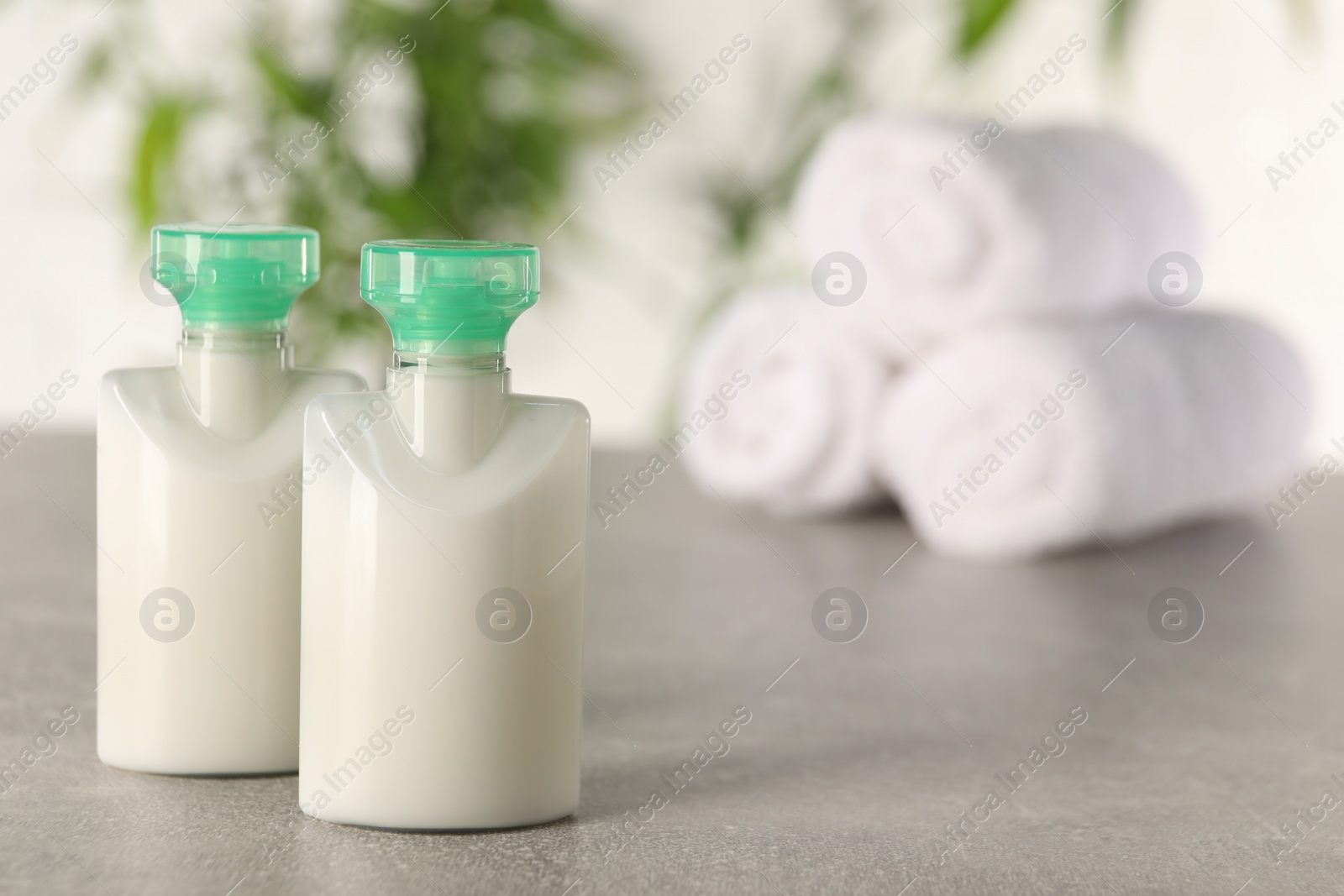 Photo of Mini bottles of cosmetic products on light grey table against blurred background. Space for text