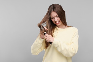 Upset woman brushing her hair on grey background, space for text. Alopecia problem