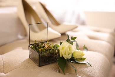 Photo of Beautiful wedding rings in glass box and flowers on textile surface indoors