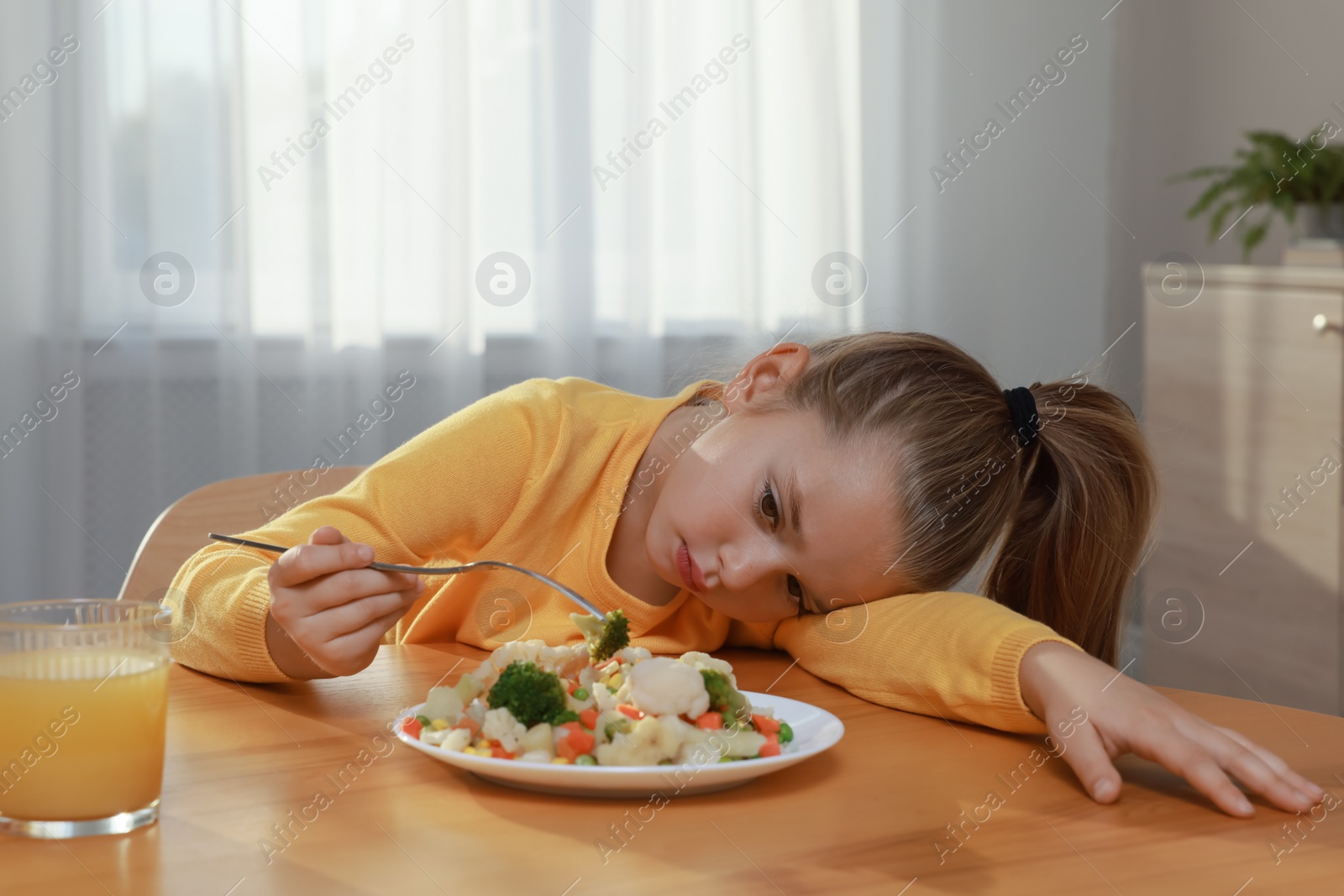 Photo of Cute little girl refusing to eat vegetable salad at home